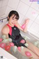 A woman sitting in a bathtub holding a bunch of balloons.