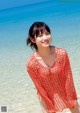 A woman standing in the water wearing a red crochet cover up.