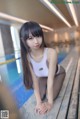 A woman in a white tank top sitting on the edge of a swimming pool.