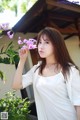 A woman in a white shirt holding a pink flower.