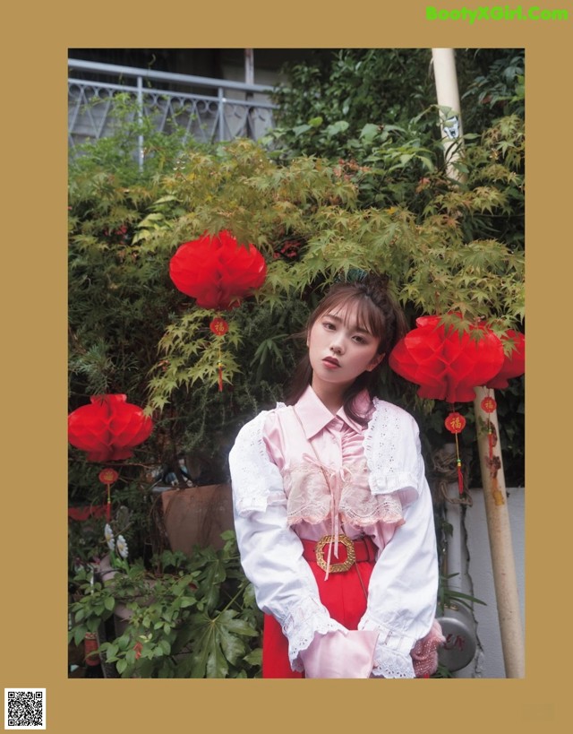 A woman standing in front of a bush with red lanterns.