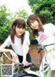 Two young women standing next to each other on a bike.