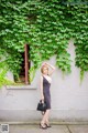 A woman standing in front of a wall covered in ivy.