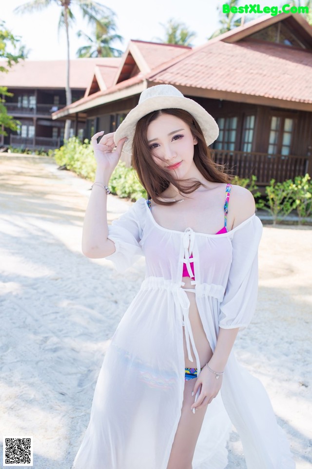 A woman in a white dress and hat posing on a beach.