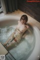 A naked woman sitting in a bathtub with water splashing around her.