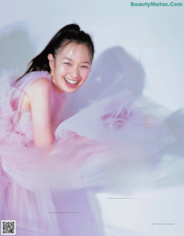 A woman in a pink dress is smiling and posing for a magazine.